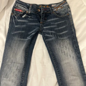 Blå Crazy Age bootcut jeans med brodyr - Snygga blå jeans från Crazy Age med bootcut passform och låg midja. Jeansen har slitningar, ljusa partier och dekorativa broderier på bakfickorna samt kontrastsömmar i gult och rött. (Har ingen dragkedja men kan användas ändå. 