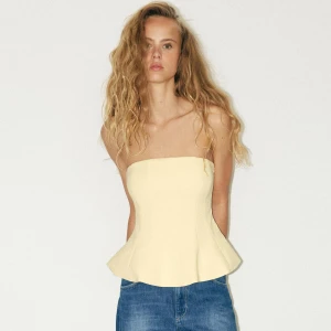 Jätte fin tub topp från Zara! - Supersnygg ljusgul bandeau korsettopp med utsvängd peplum-nederdel. Toppen är axelbandslös och har en figurnära passform som framhäver midjan. Perfekt att styla med jeans eller kjol för en trendig look.