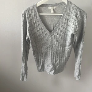 Grå kabelstickad v-ringad tröja H&M XS - Snygg grå kabelstickad tröja från H&M i storlek XS. Tröjan har v-ringning, ribbade muddar och lång ärm. Perfekt för lager-på-lager och enkel att matcha med jeans eller kjol. Mjuk och skön känsla, passar dig som gillar klassisk stil❤️