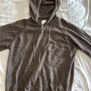 Brun hoodie med huva och snörning - Mysig marinoull brun hoodie med huva och snörning framtill. Tröjan har en klassisk känguruficka och är långärmad, perfekt för kyliga dagar. Materialet känns mjukt och skönt mot huden, och passformen är avslappnad för en chill vibe.