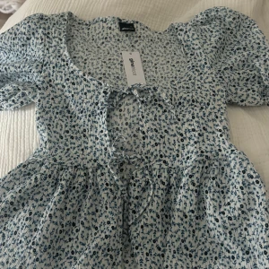 Blommig blus med puffärm Gina Tricot - Supersöt blommig blus från Gina Tricot i vitt och blått. Modellen har puffiga korta ärmar, knytning framtill och lätt volang nertill. Tunt, luftigt tyg i bomull som passar perfekt till jeans eller kjol. Sötaste toppen för vår och sommar!