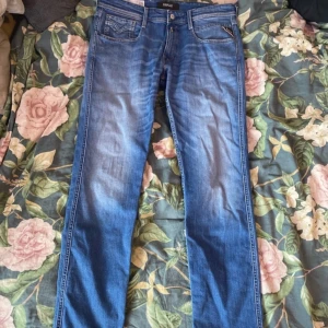Blå Replay jeans straight fit - Snygga blå jeans från Replay med klassisk femficksdesign och raka ben. Jeansen har ljusa slitningar framtill, tydliga sömmar och läderpatch bak i midjan. Materialet är jeans i bomull och passformen är normal med straight fit.