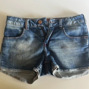 Blå jeansshorts från Levi's - Snygga blå jeansshorts från Levi's med klassisk femficksdesign och uppvikta benslut. Shortsen har låg midja, och snygga sömar som är röda. Tror original priset var nånstans runt 500 kr om inte mer. Ge gärna ett pris förslag som är rimligt. 