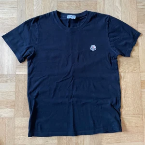  Moncler t-shirt  - Svart t-shirt från Moncler med rund hals och korta ärmar. Klassisk design med Moncler-logga broderad på bröstet. Tillverkad i mjuk bomull som känns skön mot huden. Perfekt för dig som gillar stilrena och exklusiva plagg.