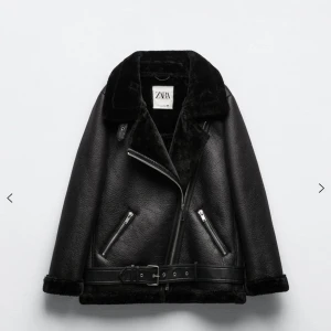 Teddy Jacka - Snygg svart pälsjacka från Zara med bred krage, dragkedjor och bälte i midjan. Jackan har mjukt foder och detaljer i skinnimitation, perfekt för kalla dagar. Stilsäker look med coola metalldetaljer och två fickor framtill.