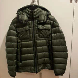  Moncler vinterjacka  - Säljer en mörkgrön dunjacka från Moncler med huva och två stora bröstfickor med lock. Perfekt för kalla dagar när du vill vara både varm och snygg. Nypris 12 000! Toppen skick, inga defekter..