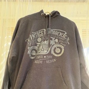 Svart hoodie med vintage motorcykeltryck - Svart hoodie från EP Collection i storlek L med coolt vintage motorcykeltryck på bröstet. Tröjan har huva med snörning och en stor magficka. Perfekt för dig som gillar streetstyle och vill sticka ut med en unik design.