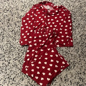Röd pyjamas med hjärtan - Mysig röd pyjamas med vita hjärtan över hela tyget. Byxorna har resår i midjan och är raka i modellen, perfekta för kalla kvällar på hösten.            100% bomull ❤️🤍