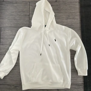 Vit hoodie från Polo Ralph Lauren XL - Säljer en stilren vit hoodie från Polo Ralph Lauren i storlek XL. Liten i storleken, mer som en storlek M. Tröjan har huva med snörning, klassisk känguruficka och den ikoniska broderade loggan på bröstet. Perfekt för dig som gillar enkel och clean streetstyle.