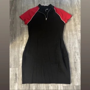 Svart och röd kortklänning från H&M  - Klänning med röda axlar och vita detaljer längs ärmsömmarna. Klänningen har korta ärmar, ståkrage och en snygg dragkedja framtill. Storlek 42, men skulle säga att den passar mindre storlekar som 38/36