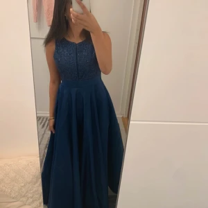 Marinblå långklänning med glitter - Säljer en marinblå långklänning med glittrig överdel och ärmlös design. Kjolen är vid och har fina veck som ger extra volym. Perfekt för dig som vill sticka ut med en elegant look och älskar glitter.