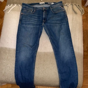 Blå Replay Rocco jeans - Snygga blå jeans från Replay, modell Rocco med klassisk femficksdesign och bekväm passform. Jeansen har tydliga kontrastsömmar, Replay-logga på bakfickan och patch i skinnimitation vid linningen. Perfekta för dig som gillar en stilren och tidlös look. Waist 33/length32