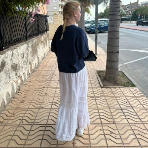 Vit långkjol  - Supersöt vit långkjol från Lindex med smockad midja och volanger. Kjolen har broderade spetsdetaljer och tunna ränder som ger en boho-vibe. Perfekt för varma dagar och chill häng. Tillverkad i mjuk bomull som känns skön mot huden.