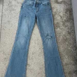 Blå bootcut jeans från ONLY, L/34 - Bootcut jeans från ONLY i ljusblå denim med slitningar på båda benen. Klassisk femficksmodell med dragkedja och knapp. Snyggt utsvängda ben och normal passform, perfekta för en avslappnad look.