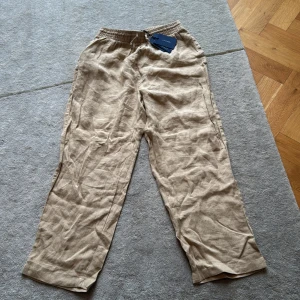 Aldrig använda beiga  linnebyxor från Gant - Snygga beiga linnebyxor från Gant med elastisk midja och dragsko. Byxorna har rak passform och är tillverkade i svalt linnematerial, perfekta för en chill och stilren look. Enkla att matcha med t-shirt eller skjorta.