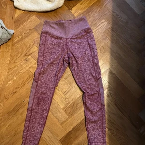 Vinröda leggings med meshdetaljer - Säljer ett par vinröda leggings med hög midja och snygga meshpaneler längs sidorna. De är stretchiga och sitter tight, perfekta för träning eller chill. Materialet är mjukt och följsamt, och färgen har en melerad look som ger extra stilpoäng.