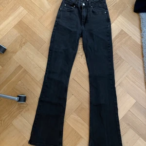 Svarta bootcut jeans från Gina - Svarta jeans från Gina Tricot i klassisk femficksmodell. Hög midja och bootcut-ben som ger en snygg siluett. Jeansen är tillverkade i stretchig denim för extra komfort och har silverfärgade nitar och knapp. Perfekta för dig som gillar en stilren look.