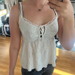 Vit linnetopp med spets och knyt - Säljer en söt vit linnetopp med spetskant vid halsringningen och smala axelband. Toppen har en lätt rynkad struktur och knyt framtill för extra detalj. Materialet känns mjukt och luftigt, perfekt för varma dagar. Passar dig som gillar romantisk och chill stil.