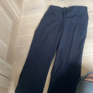 Svarta kostymbyxor från 157, stl 146 - Svarta kostymbyxor från 157 i klassisk rak modell. Byxorna har hällor för bälte, diskreta fickor bak och är tillverkade i ett mjukt tyg som känns bekvämt hela dagen. Perfekta för en clean och stilren look.