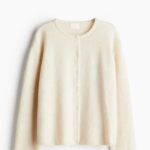 Beige kofta med knappar - Mysig beige kofta med rund halsringning och knäppning framtill. Tröjan har långa ärmar och är tillverkad i ett mjukt, stickat material som passar perfekt för kyligare dagar. Aldrig använd 