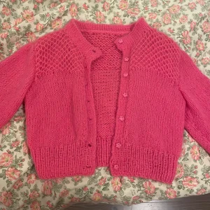 Rosa stickad kofta med knappar - Superfin rosa stickad kofta med snyggt strukturmönster upptill och ribbade muddar. Koftan har långa ärmar och stängs med matchande rosa knappar framtill. Perfekt för lager-på-lager och ger en mysig vibe till din outfit.