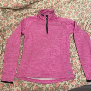 Rosa träningströja från Karhu XS - Sportig rosa långärmad träningströja från Karhu i storlek XS. Tröjan har half zip framtill, hög krage och är tillverkad i ett mjukt syntetmaterial. Perfekt för löpning eller gym, med snyggt melerat mönster och svart detalj vid ärmslut.