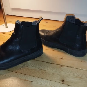 Svarta fodrade Zoe chelsea boots  - Säljer ett par svarta chelsea boots med rund tå och platt sula. Utsidan är i skinn och insidan är fodrad med mjuk grå päls för extra värme. Bootsens elastiska paneler på sidorna gör dem enkla att ta på och av. Perfekta för kalla dagar. Prisen can vi diskutera 