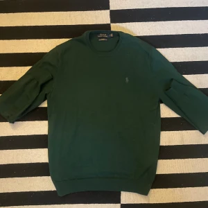 Mörkgrön merinoullströja Polo Ralph Lauren - Snygg mörkgrön tröja från Polo Ralph Lauren i tvättbar merinoull. Slim fit-modell med rund halsringning och diskret broderad logga på bröstet. Perfekt för dig som gillar klassisk och stilren look.