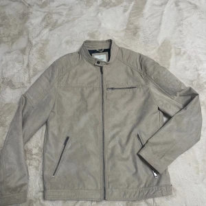 Beige mockajacka från Jack & Jones XL -  Köpt för 1200 Snygg beige mockajacka från Jack & Jones i storlek XL. Jackan har ståkrage med tryckknapp, tre dragkedjefickor och stilrena sömdetaljer. Materialet är mjukt och ger en exklusiv känsla. Perfekt för dig som vill ha en clean och modern look.