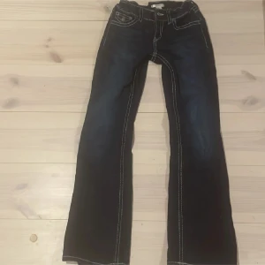 Mörkblå bootcut jeans från Gina - Snygga mörkblå jeans med bootcut passform och vita kontrastsömmar. Klassisk femficksmodell med markerade sömmar längs benen. Perfekta för dig som gillar en retrostil och vill ha ett par jeans som sticker ut lite extra.