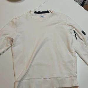 C.P. Company tröja - Vit C.P. Company tröja i storlek L. Bra skick förutom att det finns ett pyttelitet hål på ryggen som man kan se på 3 bilden som har sytts igen.