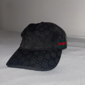 Svart zara keps med GG-mönster - Svart keps från Zara  med klassiskt GG-monogram över hela ytan och en snygg grön-röd rand på sidan. Justerbar rem bak i skinn och insida med märkning. Materialet är bomull och skinn, perfekt för dig som vill ha en lyxig streetstyle-accessoar.