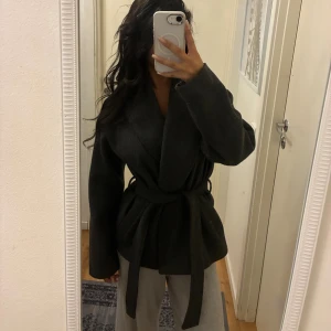 Mörkgrå omlottjacka från ONLY XS - Säljer en mörkgrå omlottjacka från ONLY i storlek XS. Jackan har bred krage, knytskärp i midjan och långa ärmar. Perfekt för dig som gillar en stilren och enkel look. Materialet känns mjukt och lite tjockare, passar bra till höst och vår.