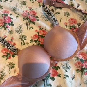 Bh Victoria's Secret - Supersnygg rosa bh från Victoria's Secret med vadderade kupor och axelband dekorerade med glittriga stenar och logga. Bh:n har en mjuk satinliknande yta och justerbara axelband för perfekt passform. Storlek 75B☺️