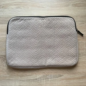Beige quiltad datorväska med dragkedja - Snygg beige datorväska med quiltat mönster och svart insida. Väskan har en guldfärgad dragkedja och ett innerfack för extra förvaring. Perfekt för att bära din laptop och tillbehör på ett stilrent sätt. Bredd 36cm, höjd 27cm. Aldrig använd. Vet ej märket.