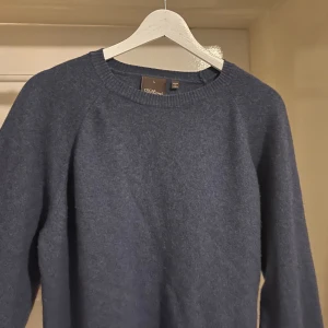 Blå stickad tröja från Oscar Jacobson - M/L. Mysig blå stickad tröja från Oscar Jacobson, tillverkad i Italien. Tröjan har rund halsringning, ribbade muddar och lång ärm. 80% ull/cashmere. Går att byta och mötas upp i Stockholm! Inga defekter vad jag kan se. 