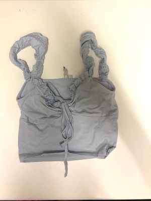 Ljusblå linnetopp med spetsband - Supersöt ljusblå linnetopp med breda axelband i spets och knytdetalj framtill. Toppen är ärmlös och har en croppad passform som passar perfekt till höga jeans eller kjol. Mjuk och skön bomullskänsla.