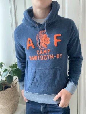 Abercrombie and fitch hoodie  - Abercrombie and fitch hoodie i blå med en orange logga. Väldigt najs och unik hoodie med ett snyggt mönster på ärmarna / slutet av tröjan. Väldigt najs och tung, sitter väldigt bra på modellen som är 180 cm 75 kg och bär Strlk S! 