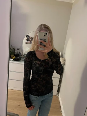 Svart spetsblus med blommönster - Säljer en svart, långärmad spetsblus med blommigt mönster. Toppen är genomskinlig och har en tight passform som framhäver figuren. Perfekt för dig som vill ha en trendig och edgy look. Knappt använd och är storlek M men passar mig som oftast bör S💗
