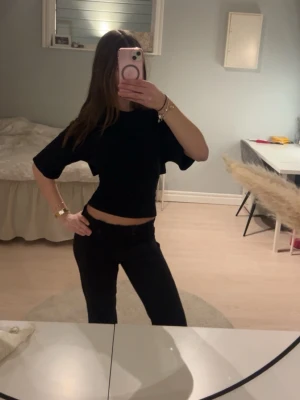 Svart croppad topp med knyt i ryggen - Säljer en svart croppad topp med korta ärmar och snygg knytning i ryggen. Toppen har en loose passform och är perfekt för dig som vill ha en enkel men ändå trendig look. Passar till både jeans och kjol.