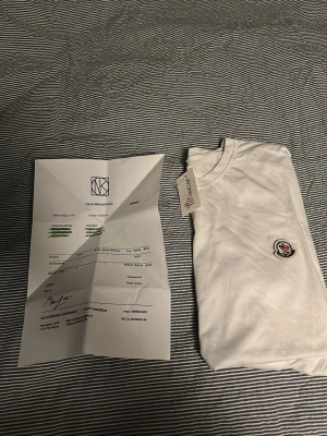 Vit Moncler t-shirt med logga - Snygg vit t-shirt från Moncler med klassisk rund hals och Monclers ikoniska logga broderad på bröstet. T-shirten har korta ärmar och är tillverkad i mjuk bomull för en skön känsla. Perfekt för dig som gillar stilrena och exklusiva plagg.