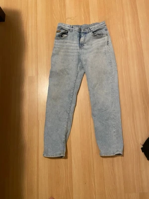 Ljusblå raka jeans i klassisk modell - Säljer ett par ljusblå jeans med rak passform och klassisk femficksdesign. Jeansen har hög midja och är tillverkade i bomull med en typisk jeansstruktur. Perfekta för en avslappnad och stilren look.