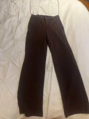 Bruna vida kostymbyxor - Snygga bruna kostymbyxor med vida ben och klassisk passform. Byxorna har bälteshällor och stängs med dragkedja och knapp. Perfekta för en stilren look och passar till många olika outfits.