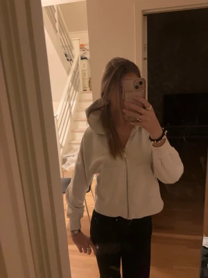 Vit hoodie med dragkedja - Snygg vit hoodie med dragkedja framtill och huva. Modellen är croppad och har långa ärmar med muddar. Perfekt för en avslappnad och trendig stil.