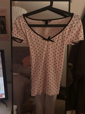 Prickig topp med rosett  - Söt ljusrosa topp med svarta prickar, v-ringning och en liten rosett framtill. Svarta kantband vid hals och ärmslut ger en fin kontrast. Så skön! Postar på mindre än 24h🤗jag har sytt den så passar för dig som har storlek xs-s