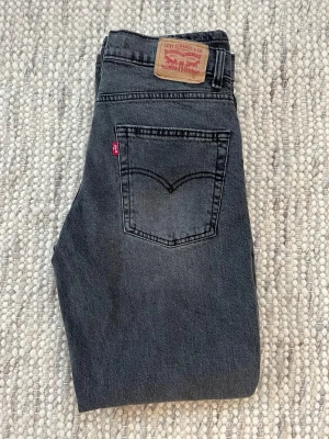 Levi's 501 grå jeans straight fit - Snygga grå Levi's 501 jeans med klassisk straight fit och femficksmodell. Jeansen har en mörkgrå tvätt, ikonisk läderpatch bak och är tillverkade i slitstark bomullsdenim. Passar en person som är mellan 165-180 cm 