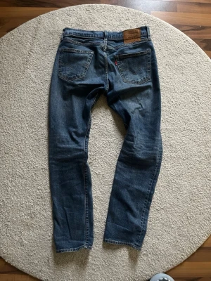 Levi's 511 blå jeans herr - Snygga blå Levi's 511 jeans med klassisk femficksdesign och läderpatch bak i midjan. Jeansen har en smal passform och är tillverkade i slitstarkt denimtyg av bomull. Perfekta för en avslappnad och trendig look.
