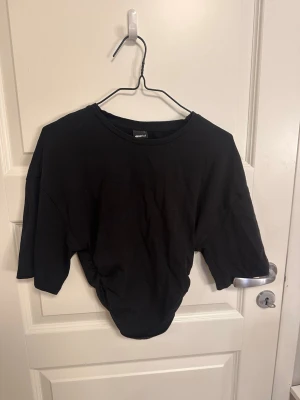 Svart croppad t-shirt Gina Tricot - En svart croppad t-shirt från Gina Tricot i mjuk bomull. Klassisk rund halsringning och korta ärmar. Perfekt till höga jeans eller kjol för en enkel och clean look.