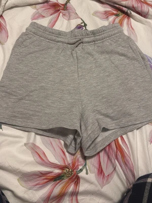 Grå mjuka shorts med snörning från lager157 - Gråa shorts i mjukt material med elastisk midja och snörning. De har praktiska sidofickor och en avslappnad passform, perfekta för varma dagar eller chill hemma. Passar mig som är en storlek S. Nya oanvända men ingen lapp då jag rev av den. Ordinariepris 100kr