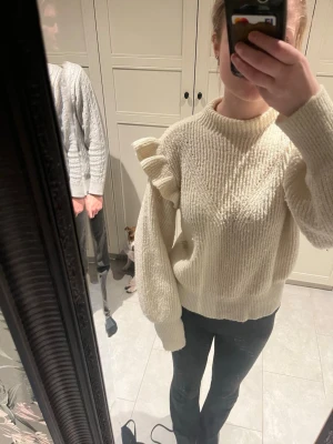 Krämvit stickad tröja med volang Vila - Säljer en krämvit stickad tröja från Vila med volangdetalj på båda  axeln. Tröjan har rund halsringning, ribbade muddar och är gjord i ett mjukt, fluffigt material. Perfekt för dig som gillar trendiga detaljer och vill ha något extra i garderoben. Pris diskuteras gärna! 